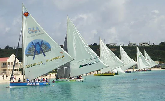 Traditional wooden sailing boats racing off the coast of Anguilla with crowds watching from the beach