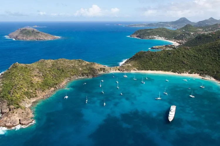 Secluded Colombier Beach in Saint Barthelemy surrounded by green hills and turquoise water with sailboats anchored