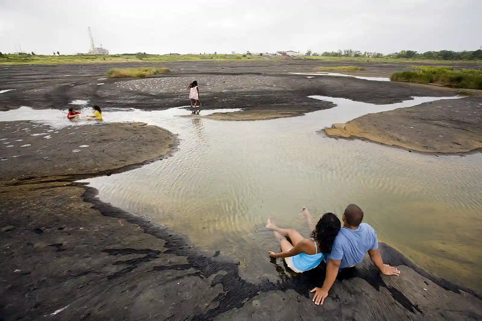 Grey wrinkled surface of La Brea Pitch Lake with small pools of water, Trinidad