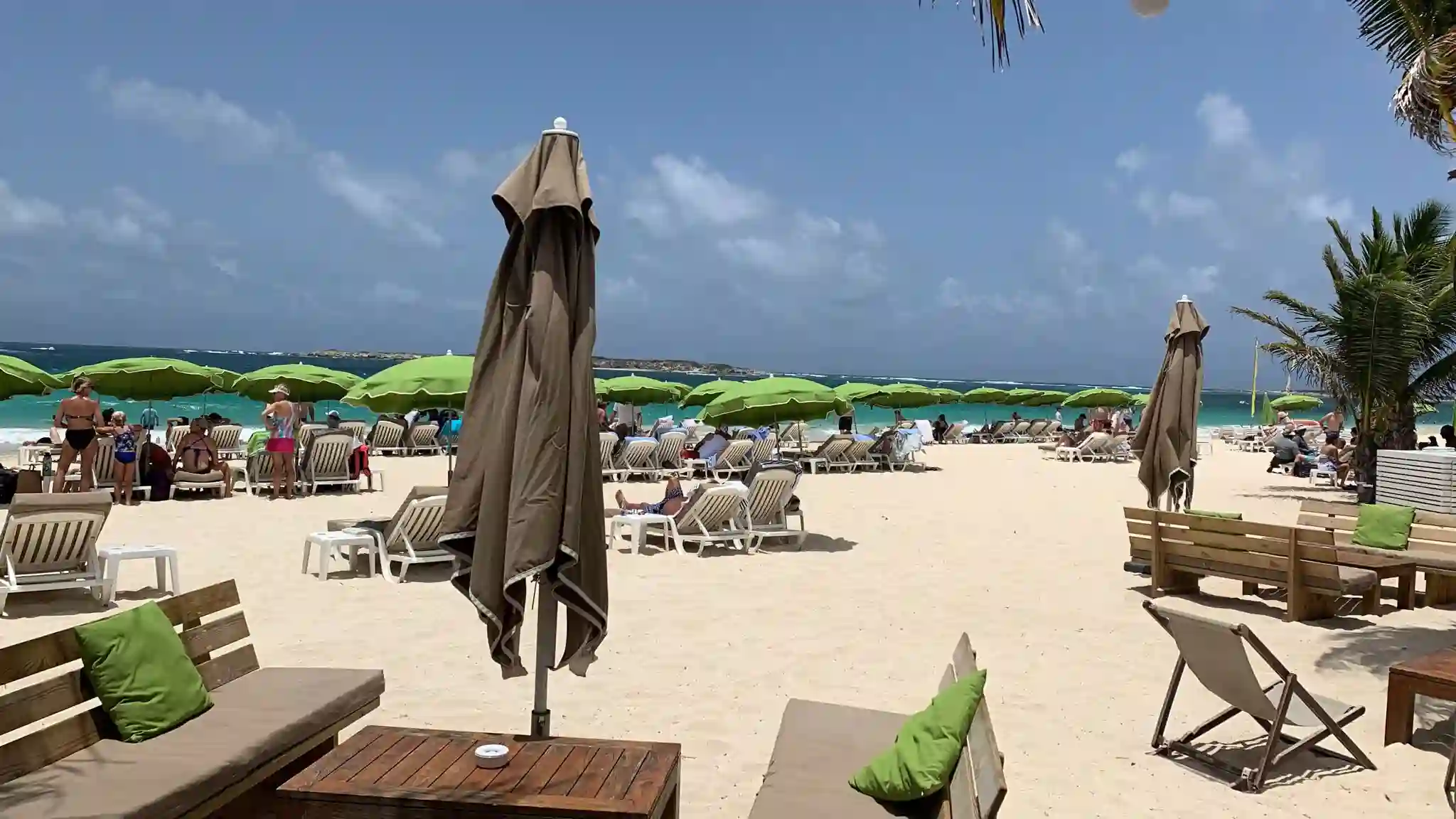 Long white sand beach at Orient Bay, Saint Martin, with colorful loungers, umbrellas and turquoise water