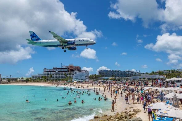 Large passenger jet flying low over crowds on Maho Beach as it lands at Princess Juliana Airport, Saint Martin