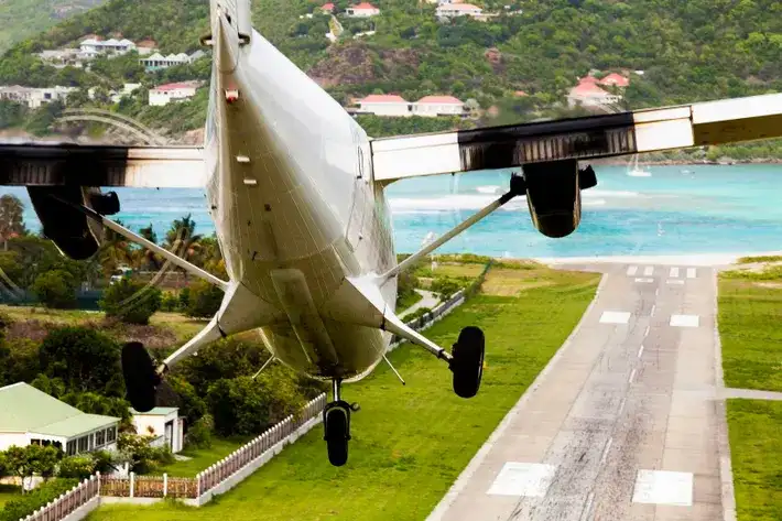 Small propeller plane descending steeply over a hilltop road toward the short runway at Saint-Jean airport, Saint Barthelemy