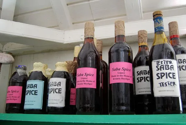 Bottle of homemade Saba Spice spiced rum liqueur with a small glass on a wooden table